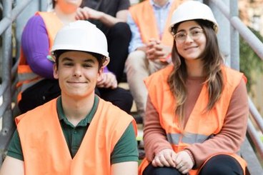 una studentessa e uno studente con caschetto e giubbotto ad alta visibilità